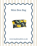 A mini box bag with a black background and a yellow lemon and green leaf floral pattern, shown on a white card with a blue scalloped border and the text 'Mini Box Bag' and 'www.kaalimadeit.