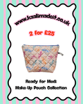 A quilted make-up pouch with a pastel multicolor lizard print on a pink background, presented on a white card with pink and mint striped borders. The card features text reading 'www.