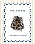 A mini box bag with a beige and black leopard print pattern, shown open to reveal its gold-toned interior. The image is presented on a white card with a navy blue scalloped border, featuring the text 