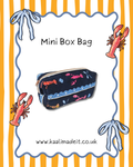 A navy blue mini box bag with a pink, orange, and white lobster print, shown on a white background with a wavy blue border, orange and yellow stripes, lobster illustrations, and the text 'Mini Box Bag' and 'www.kaalimadeit.co.uk